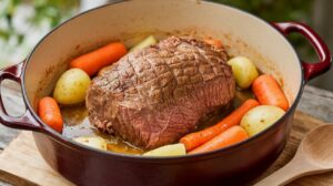 Dutch oven pot roast with tender beef, carrots, potatoes, and gravy served in a rustic cast iron pot.

