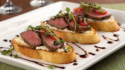 Beef Tenderloin Crostini Delight: Close-up of toasted baguette topped with tender beef slices, creamy sauce, and fresh garnishes.