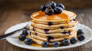 A stack of fluffy homemade pancakes topped with fresh berries and a drizzle of maple syrup on a rustic plate.