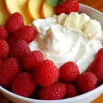 A bowl of creamy cream cheese fruit dip served with fresh fruit like strawberries, grapes, and apple slices.