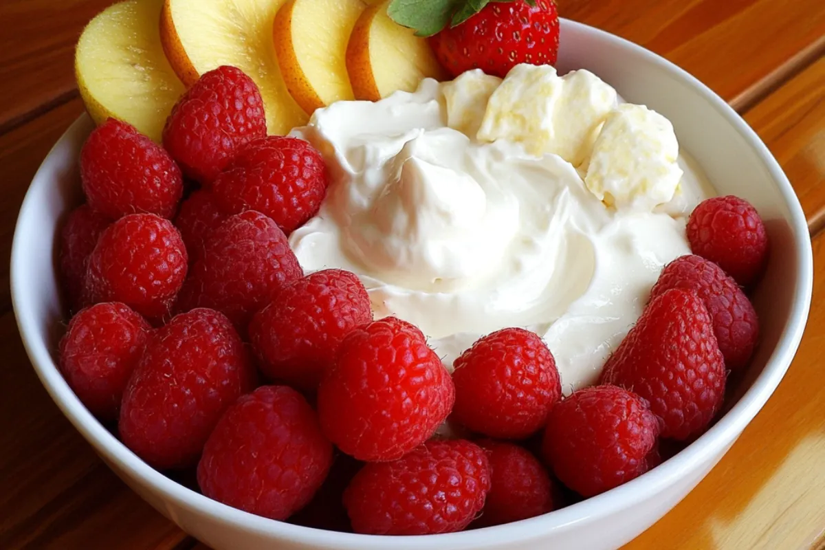 A bowl of creamy cream cheese fruit dip served with fresh fruit like strawberries, grapes, and apple slices.