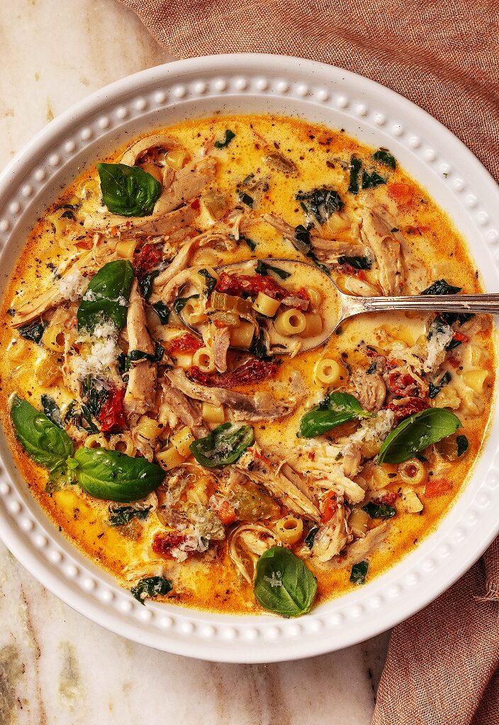 Ultra-realistic creamy chicken soup with shredded chicken, sun-dried tomatoes, spinach, and herbs in a ceramic bowl, studio lighting, neutral background