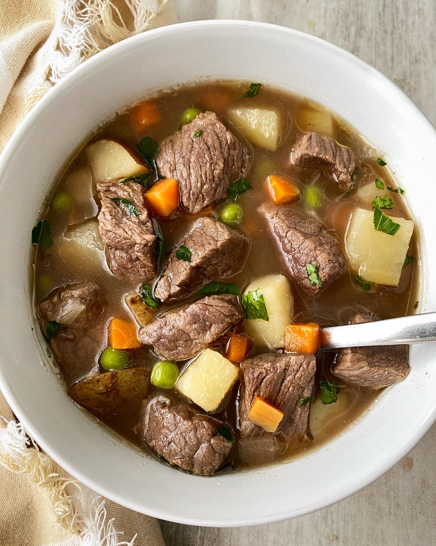 Ultra-realistic steak and potato soup with beef pieces, diced potatoes, carrots, celery, and onions in a creamy broth, served in a ceramic bowl, studio lighting, neutral background