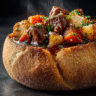 Ultra-realistic spicy beef stew with dark glossy broth, beef chunks, carrots, potatoes, and onions served inside a crusty bread bowl, steam rising, studio lighting, dark background